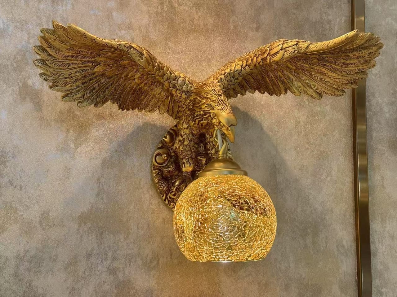 Gold eagle wall sconce with decorative glass shade on a textured wall.