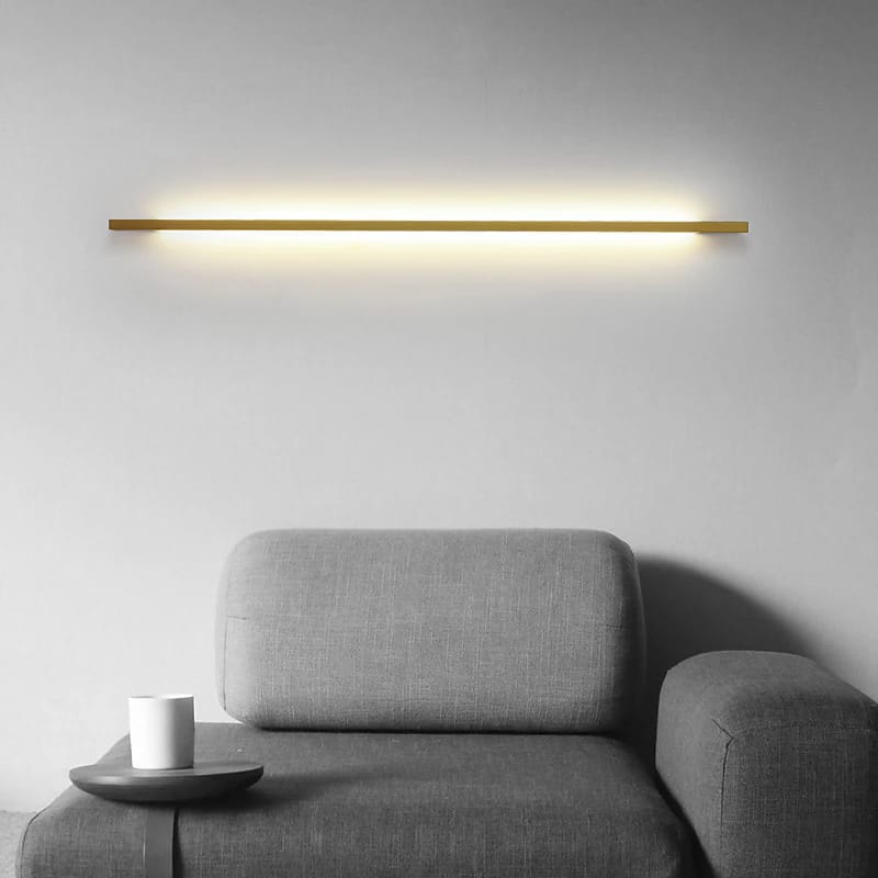 Modern wall light fixture above a gray sofa in a minimalistic room.