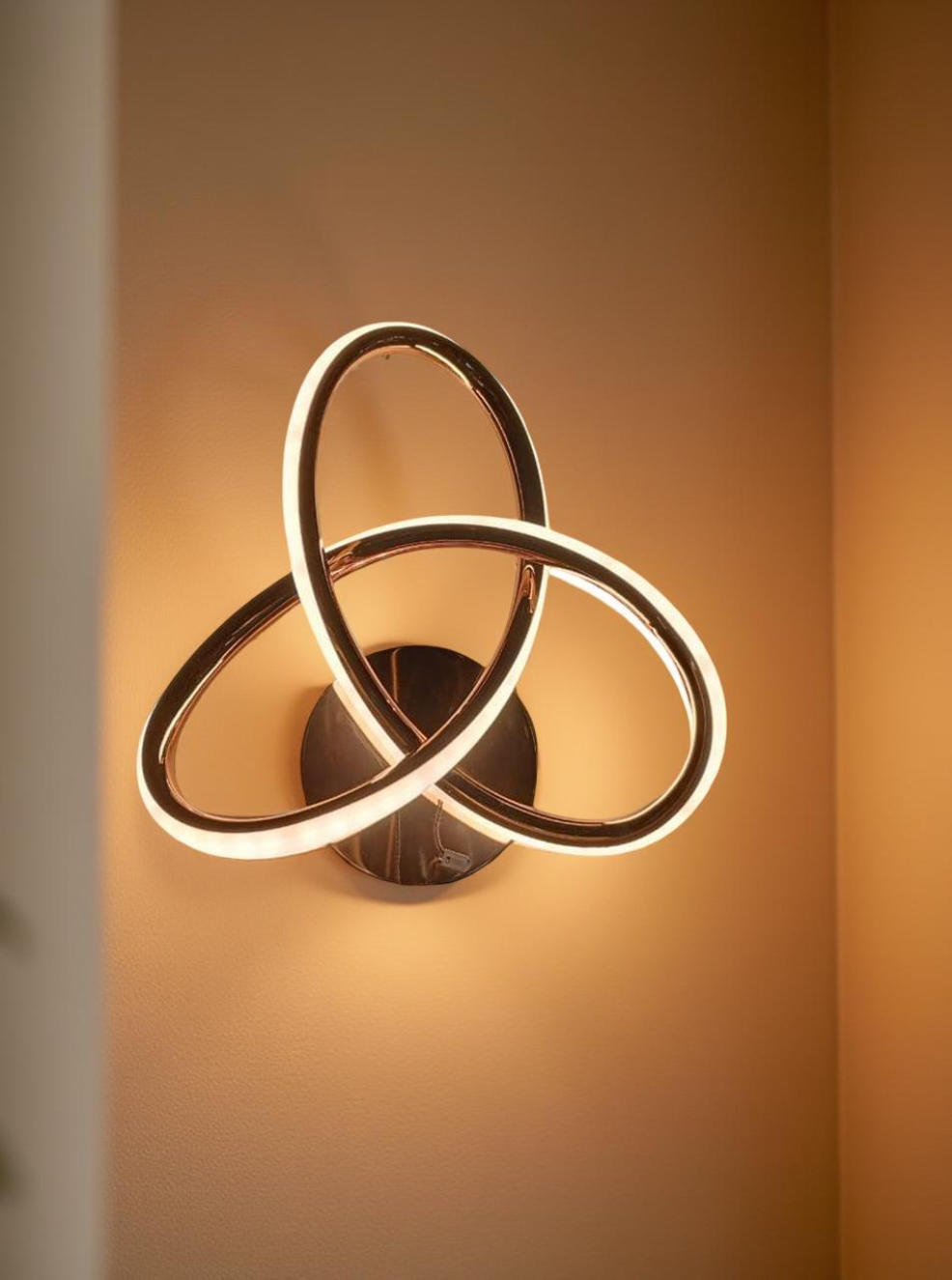 Modern wall light fixture with three interlocking rings on a warm-toned background