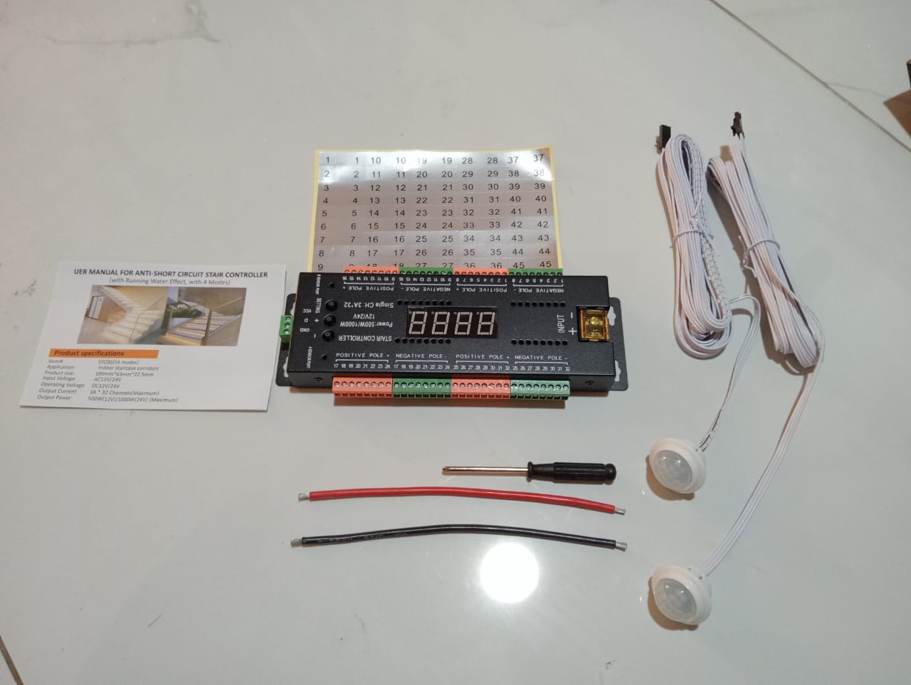 Electronic control board with digital display, wires, and tools on a white surface