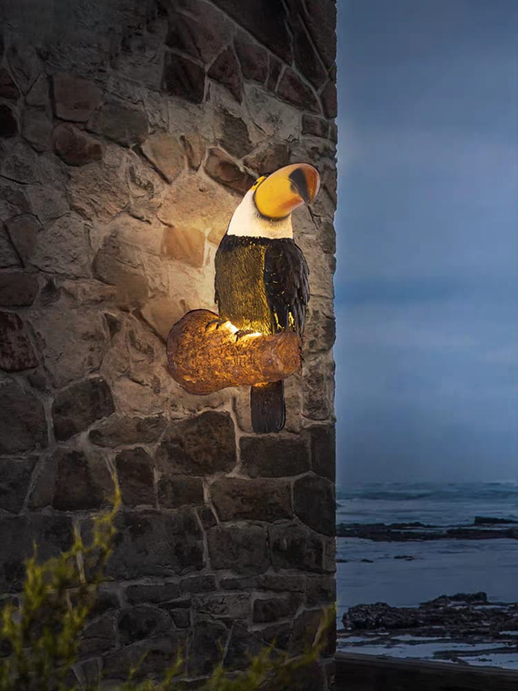 Decorative lamp shaped like a toucan on a stone wall with ocean view
