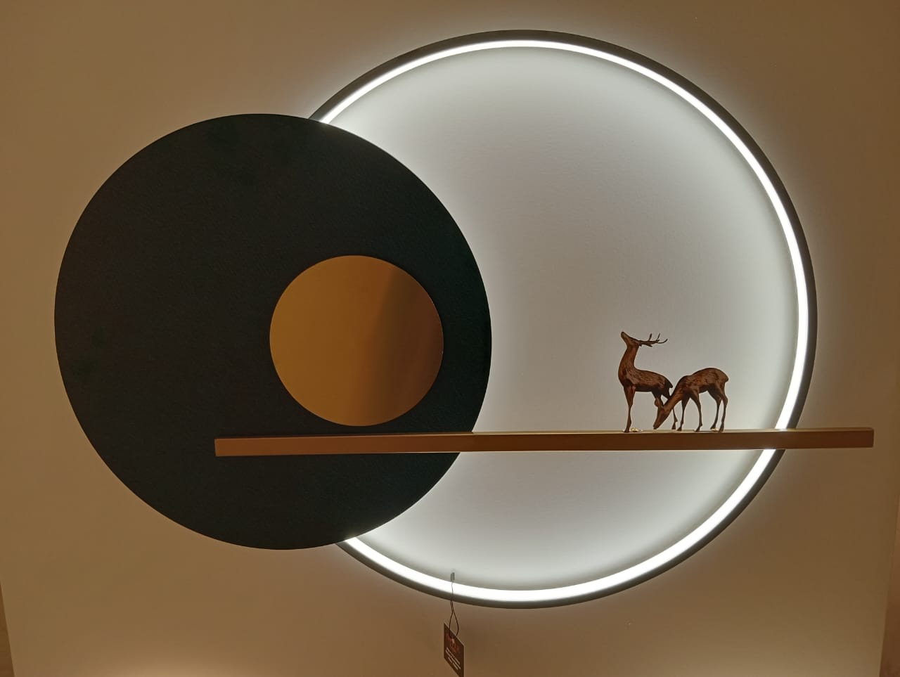 Decorative wall art with a black circle, orange circle, and two deer silhouettes on a white background.