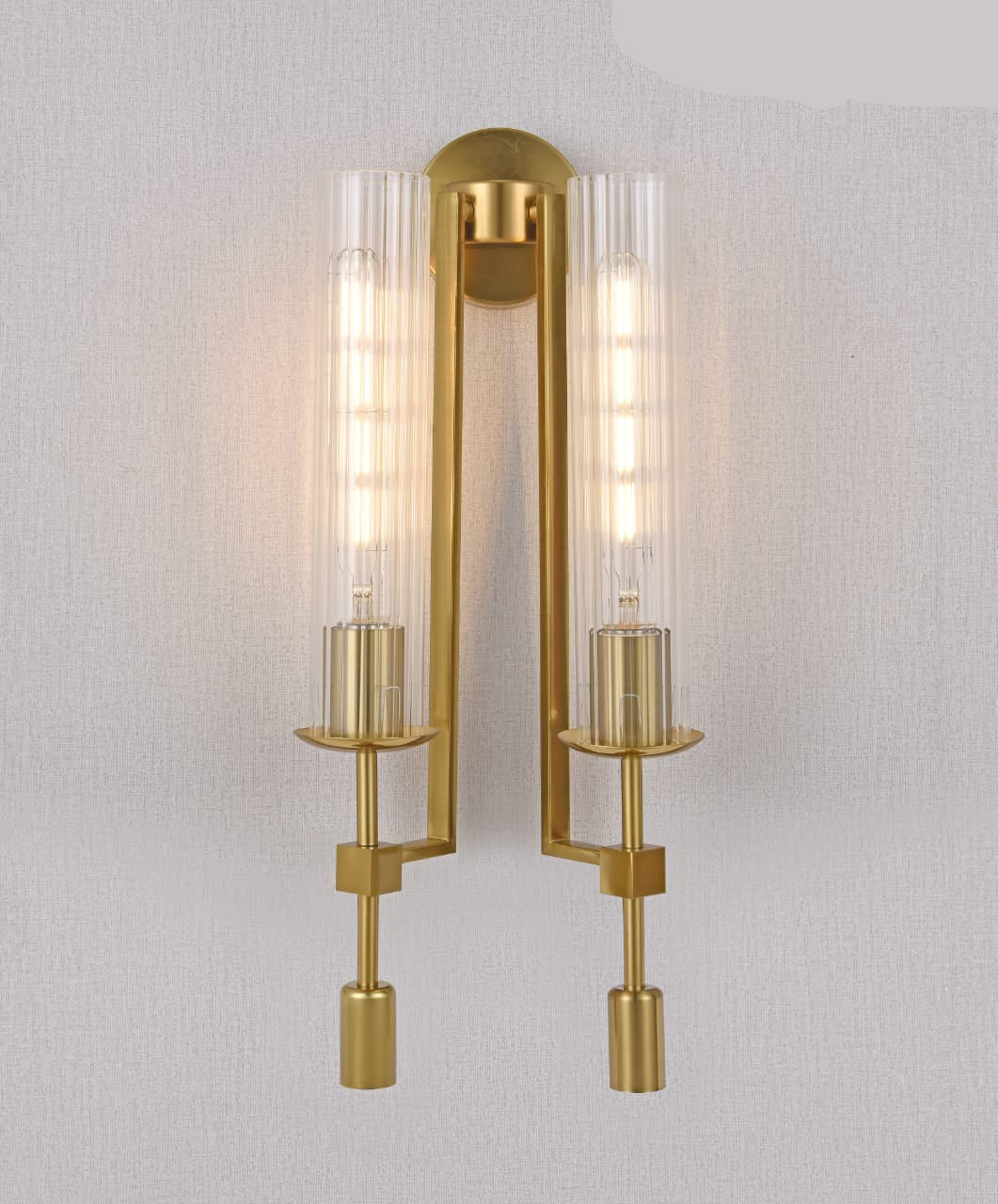 Gold wall sconce with clear glass shades on a light gray background