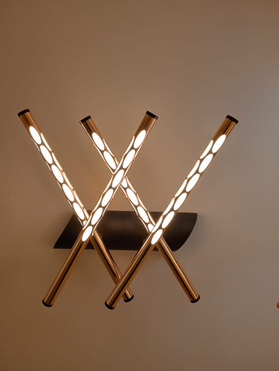 Modern wall light fixture with three gold cylindrical arms on a neutral background