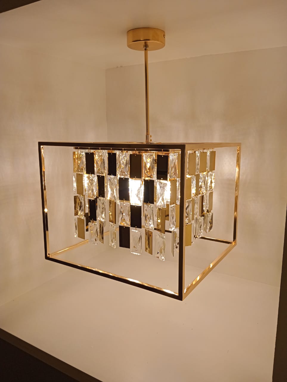 Modern chandelier with glass blocks and gold frame on a plain wall.