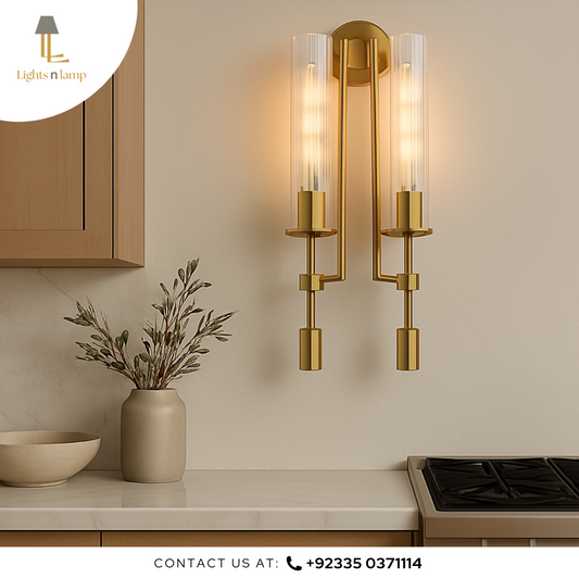 Gold wall sconce fixture on a kitchen wall with a vase and plant on the counter.