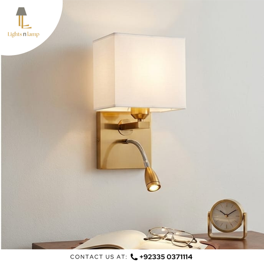 Gold wall sconce with reading light on a white wall, next to an open book and glasses.