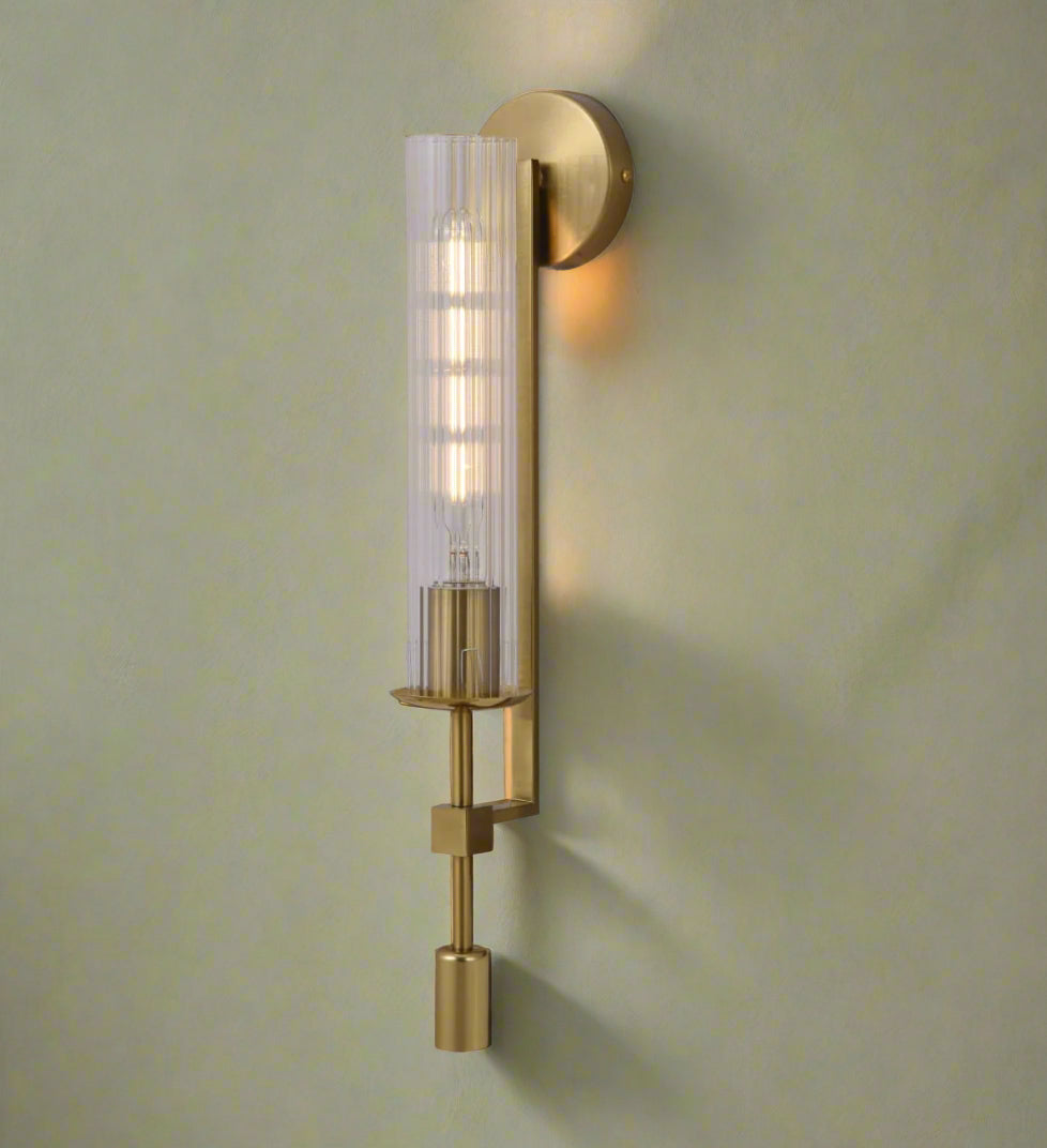 Gold wall sconce with a clear glass shade on a green wall